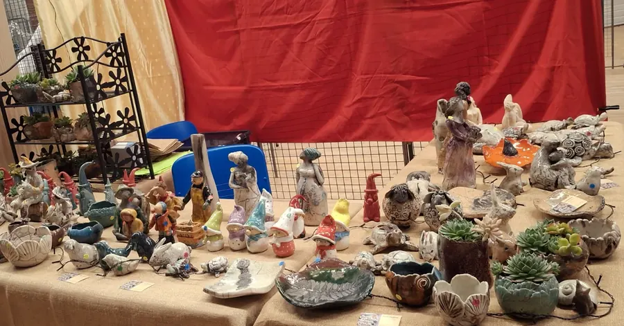 Le stand de Terres mêlées devant une tenture rouge : des dizaines de personnages, d'animaux, de bols et de pots à succulentes alignés sur une toile de jute.